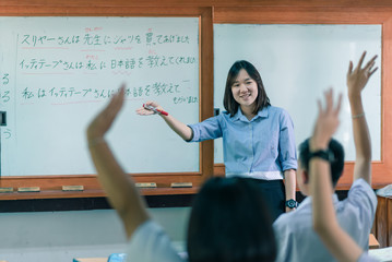 An Asian female teacher is teaching Japanese. The meaning of texts are "Mr. Suriya bought a shirt for the teacher, Mr Ittithep taught me Japanese, I have been taught Japanese from Mr Athithep".