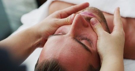 Close up of an young handsome man is receiving a facial massage and spa treatment for perfect skin in a luxury wellness center.