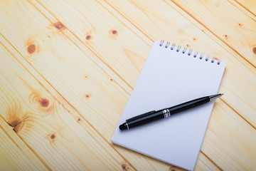 A memo paper notebook with black pen over wooden texture background, table blank space. Beginning of new goals and new year resolution concepts.