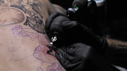 Close up tattoo artist demonstrates the process of getting black tattoo with paint on back of a client