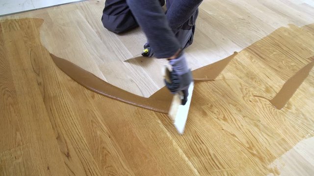 Carpenter master with gloves grouting wooden parquet, phase after sanding. Varnishing of oak parquet floor, man workers with hand and spatula