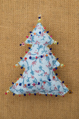 Handmade blue textile cotton fabric naive retro style Christmas tree ornament decorated with beads on burlap background
