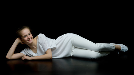 Fototapeta na wymiar Cute little girl lying on the floor in the studio on a black bac