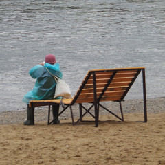 Back view of a fisherman. Seated fisherman in a raincoat. Fishing rod. 