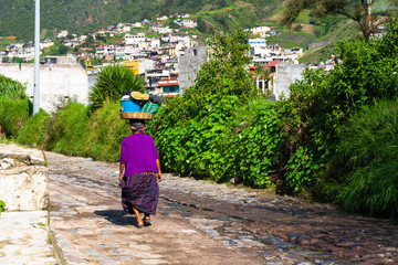 La señora está caminando con una cesta en la cabeza por una calle de Almolonga Guatemala.
