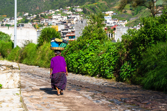 La se&ntilde;ora est&aacute; caminando con una cesta en la cabeza por una calle de Almolonga Guatemala.