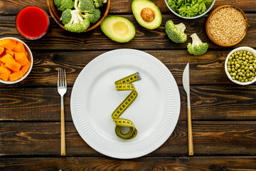Obraz na płótnie Canvas Diet program concept. Empty plate, measure tape and vegetables on dark wooden background top view