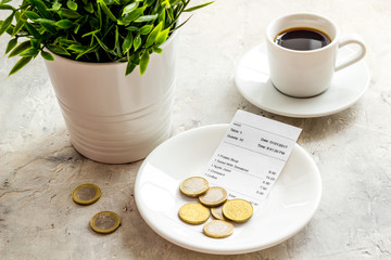 Pay restaurant bill by cash. Reciept and coins on plate on grey background