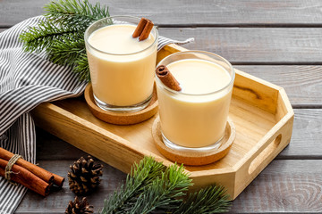 Drink eggnog on dark wooden New Year table decorated with spruce branches and gingerbread