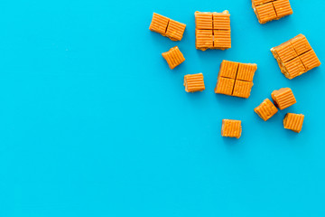 Caramel candies cubes on blue background top view frame copy space