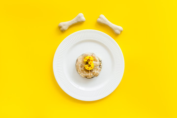 Birthday party for puppy concept. Dog feed, candle in shape of number three, bones on yellow background top-down