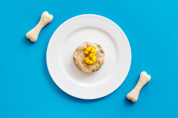 Birthday treat for puppy concept. Dog feed, candle in shape of number three, bones on blue background top-down