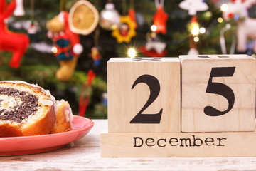 Date 25 December on cube calendar, poppy seeds cake and christmas tree with decoration