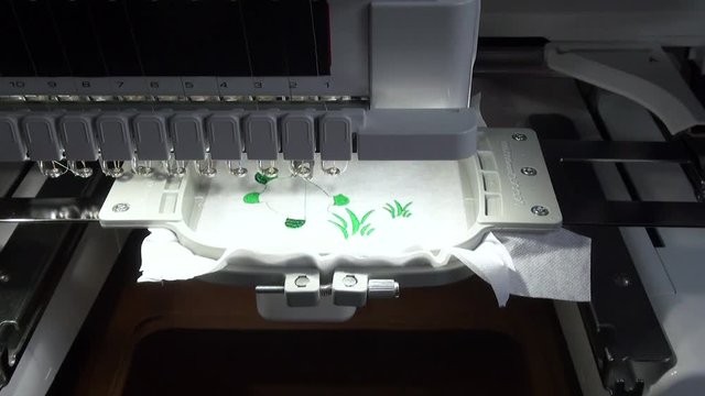 start  and stop of work of the embroidery machine with the green  thread   when performing work on the automated production of a colored design turtle and  grass on the white  background