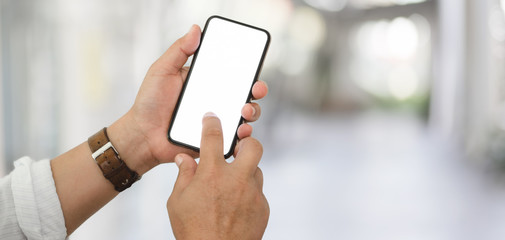 Cropped shot of businessman using his blank screen smartphone with blurred office background
