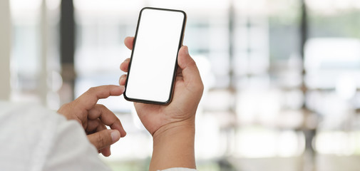 Cropped shot of businessman using his blank screen smartphone with blurred office background