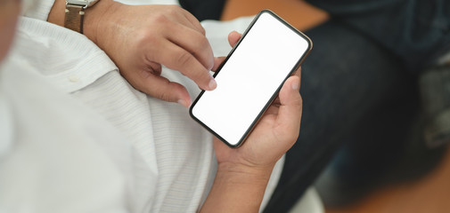 Cropped shot of man using his blank screen smartphone while sitting in comfortable room