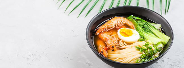 Asian noodle soup, ramen with prawn shrimp, vegetables and egg in black bowl on gray concrete background. Flat lay, Top view, mock up, overhead. Healthy food concept