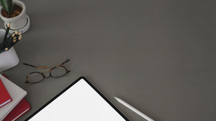Top view of trendy workplace with tablet and office supplies on dark grey table background