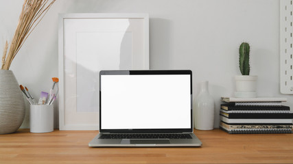 Cropped shot of comfortable workplace with laptop computer and office supplies on wooden table background and white wall