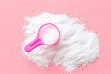 Washing powder in plastic spoon on pink background top view