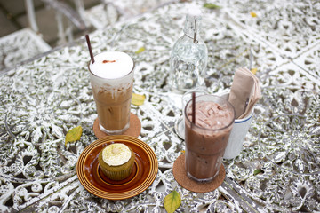 Iced cold brew cappuccino coffee in a glass and iced chocolate with green tea muffins and cream on vintage table.