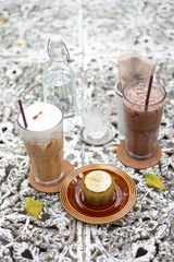 Iced cold brew cappuccino coffee in a glass and iced chocolate with green tea muffins and cream on vintage table.