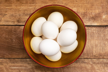 Chicken eggs lie in a wooden bowl. A bowl stands on a wooden background. View from above.