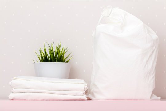 Close-up of a stack of white bedding, storage bag, house plant on a table against the background of light wall