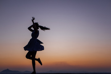 Silhouette of a young dancing woman with long wavy hair in the mountains , Natural light and darkness,against the background of the sunset sky.