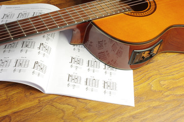 Obraz na płótnie Canvas Acoustic guitar and chord book on a wooden texture