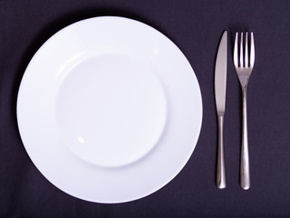 white plate, knife and fork on napkin on dark tablecloth
