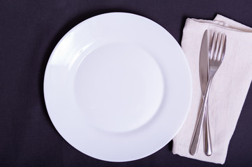 white plate, knife and fork on napkin on dark tablecloth