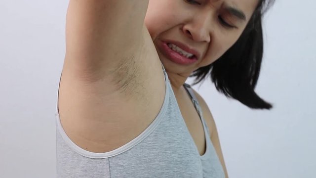 Close up of young woman showing her unshaved armpit and offensive face isolated on grey background. Concept of Health care for skin and beauty.