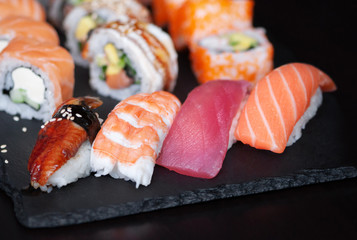 Japanese nigiri sushi and rolls with unagi, srimp, tuna and salmon on black stone plate.