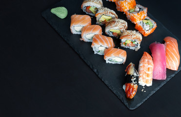 Sushi set with nigiri sushi, uramaki California, Philadelphia, Unagi rolls on stone plate. Top view, black background.
