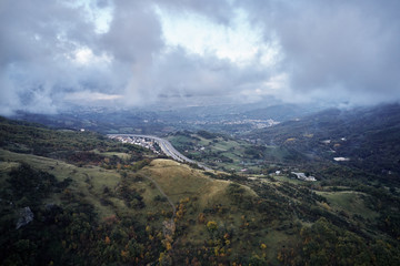 Autumn alpine speed road in Italia. Aerial view from above with clouds on the background and village far away