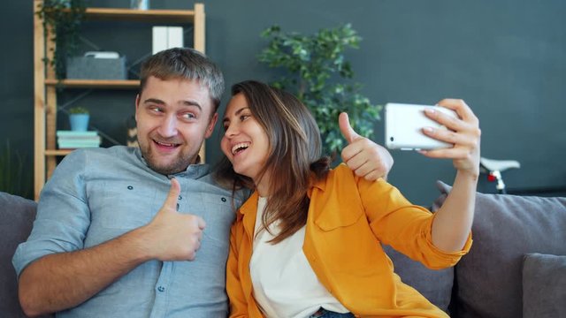 Man and woman taking selfie with smartphone having fun laughing kissing enjoying funny activity at home. Technology, happy youth and photograph concept.