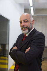 Cheerful mature businessman in office. Professional mature businessman standing with crossed arms and smiling at camera in office. Leadership concept