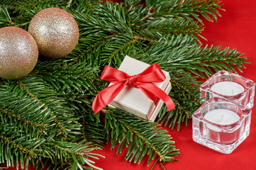 Fototapeta na wymiar New Year's composition, Christmas decorations. Gift box in white packaging with a red bow next to Christmas sparkling balls, fir-tree branch on a red velvet background. With copy-space