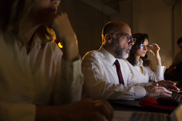 Obraz premium Focused coworkers working in dark office. Cropped shot of professional male and female business people working with computers late at night. Business and technology concept