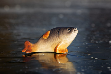 Porcelain fish stands on smooth ice of frozen pond. Goldfish from fairy tale, wish fulfillment
