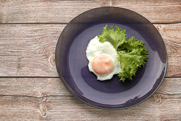 Appetizing fresh scrambled eggs with green lettuce leaves on a purple plate on a wooden background. Selective focus. The view from the top. Delicious Breakfast. A proper dinner