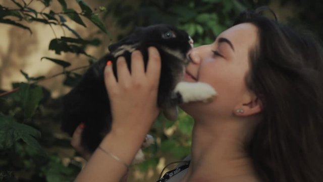 Close side view of young beautiful woman kissing cute little bunny outdoor