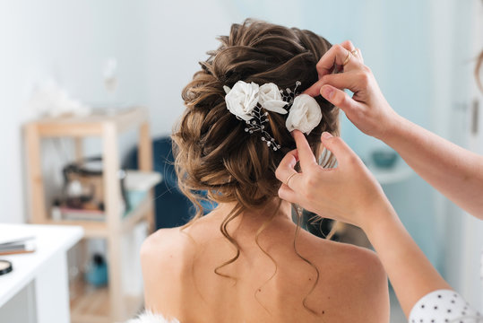 hairdresser makes an elegant hairstyle styling bride with white flowers in her hair