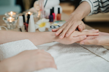 Obraz na płótnie Canvas Beauty therapist doing manicure on hand of young asian woman in spa salon. closeup view of two female hands while beautician massage customer hands skin with moisturizing lotion before nail polishing