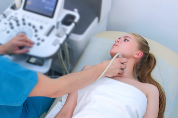 Man doctor examining patient's young woman thyroid gland using ultrasound scanner machine. Doctor runs ultrasound sensor over patient's neck and looking at screen. Diagnostic examination.