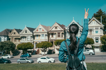 back view portrait of young girl with backpack showing v sign while raising hands. female tourist...