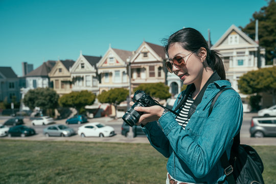 travel female photographer taking picture on vintage camera of scene Painted Ladies in San Francisco. young girl tourist checking photo standing under blue sunny sky on meadow. pretty asian woman.