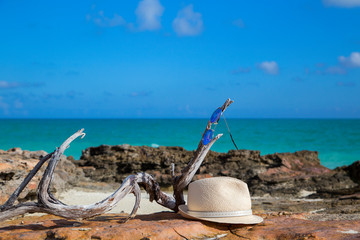 A man's straw hat and sunglasses lie against the beautiful sea.Horizontally.